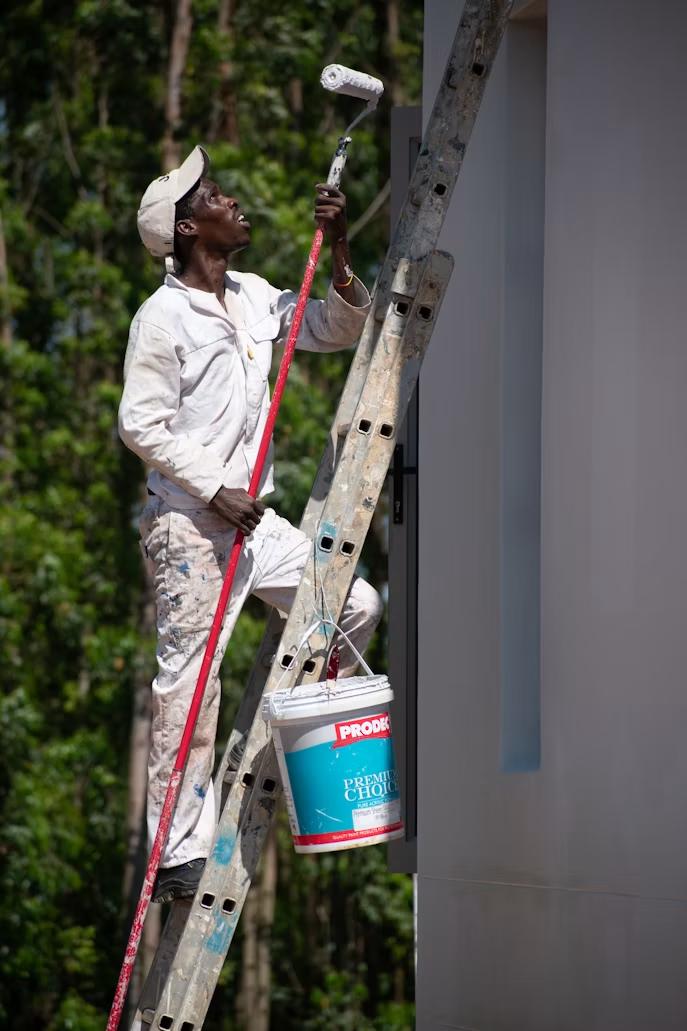 a painter on a ladder painting the outside of a house