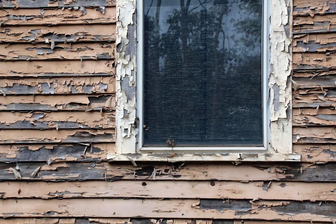 peeling paint on weathered wooden siding of the house
